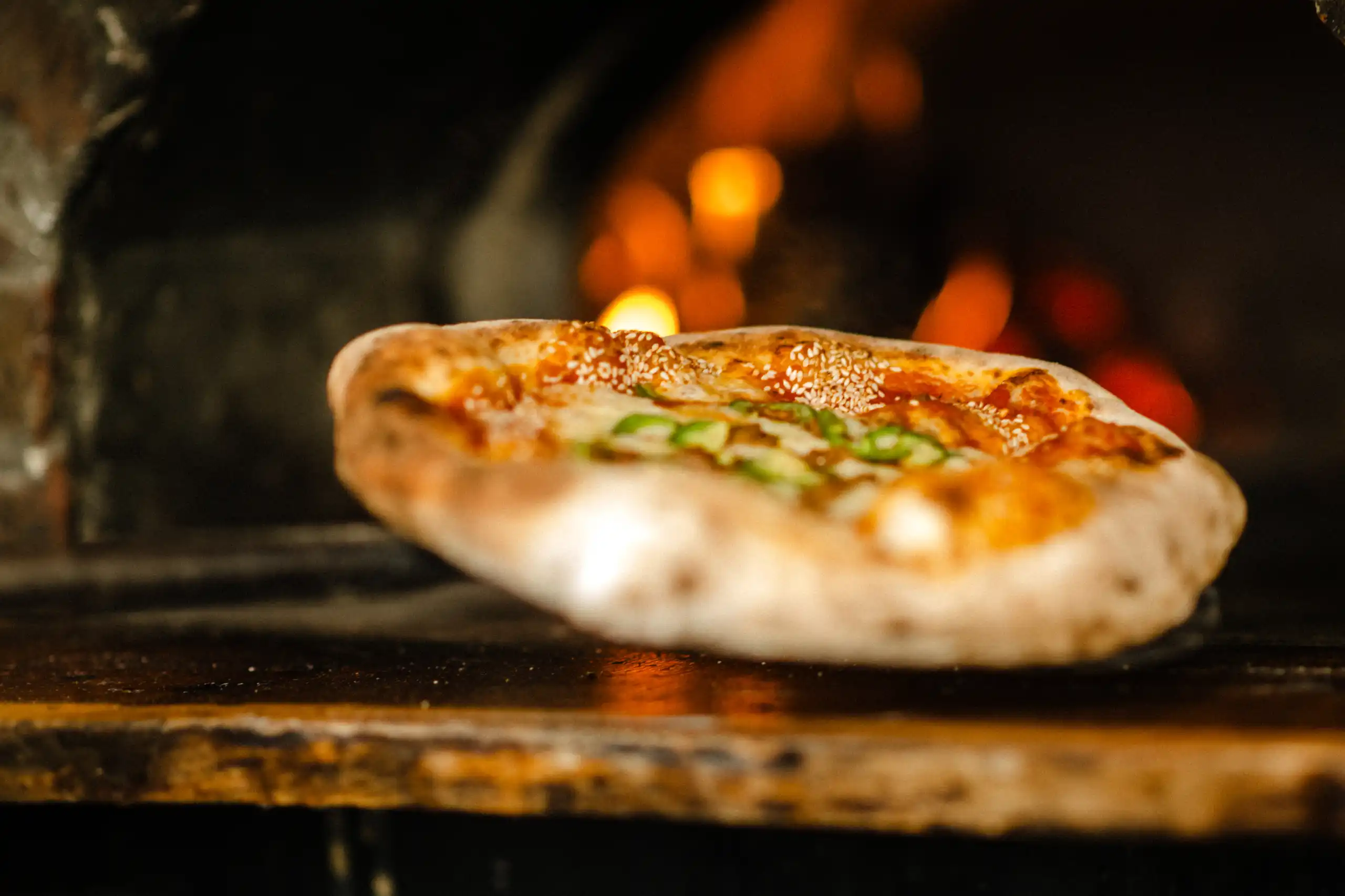 A wood-fired pizza coming out of the oven